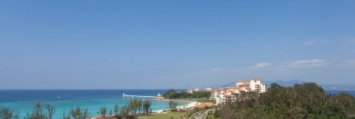White buildings with orange roofs stand beside a clear blue ocean under a vast, cloudless sky.