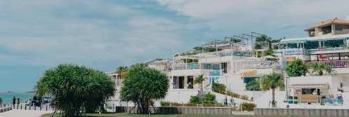 Tiered white concrete buildings with open terraces sit beside tropical greenery on Kouri Island in Okinawa.