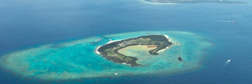 An oval island sits within a shallow turquoise reef surrounded by deep navy ocean waters in Okinawa.