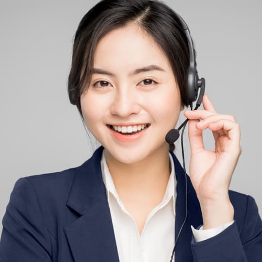 A smiling woman in a navy blazer and white shirt wears a black headset against grey.
