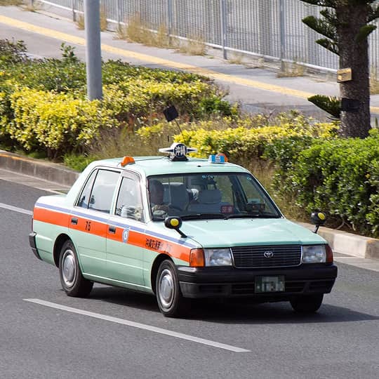 A pale green sedan with an orange stripe travels along an asphalt road in Okinawa.