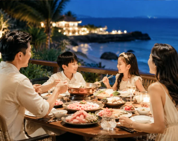 A family shares a hot pot dinner on an outdoor wooden terrace overlooking the evening ocean.