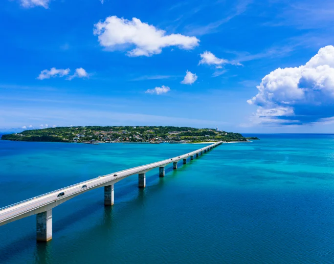 A long concrete bridge spans across deep indigo waters toward the lush greenery of Kouri Island, Okinawa.