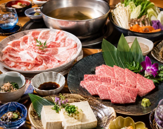 Thinly sliced pork and marbled beef are arranged on ceramic plates beside a steaming metal hot pot.