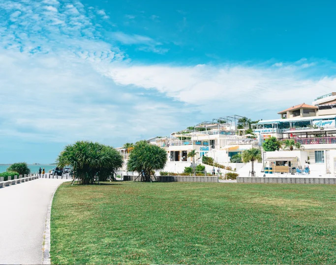 A paved path borders a green lawn leading to white multi-level buildings under a bright blue sky.